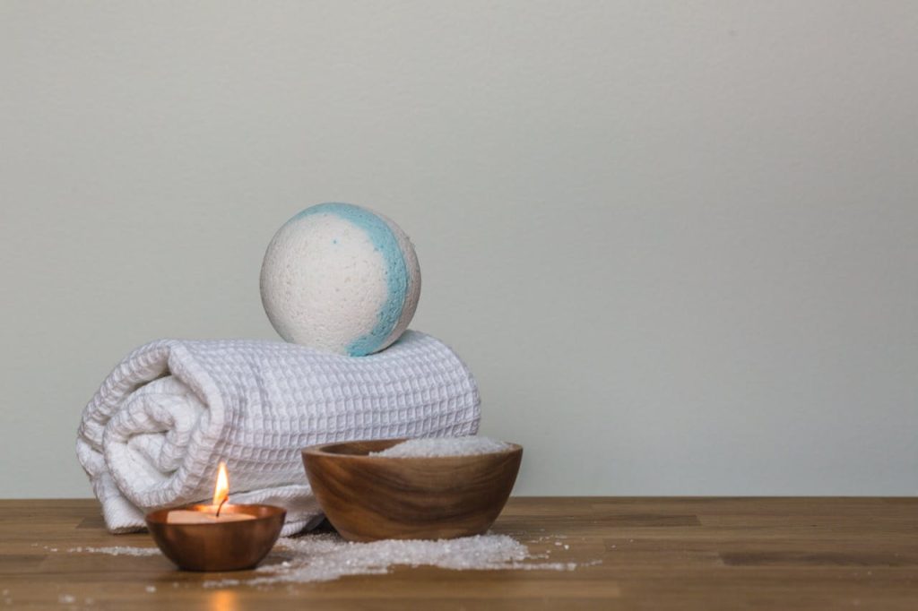 Peaceful spa setting with bath bomb, salt, candle, and towel, perfect for relaxation.